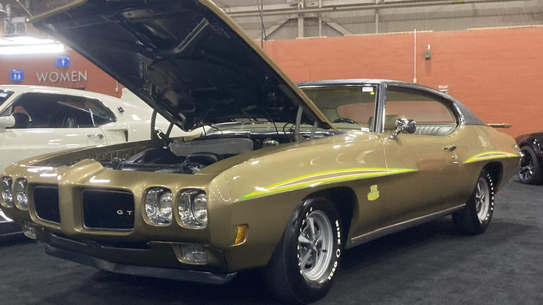 Pontiac GTO 1970 года, припаркованный в помещении на автосалоне, с открытым капотом, вид спереди слева в 3/4