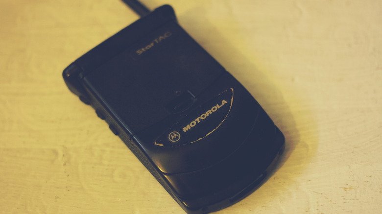 Черный раскладной телефон Motorola StarTAC, лежащий на деревянной поверхности.