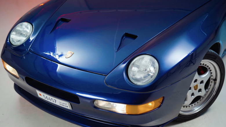 Передняя часть редкого синего Porsche 968 Turbo S крупным планом под студийным освещением в гараже.
