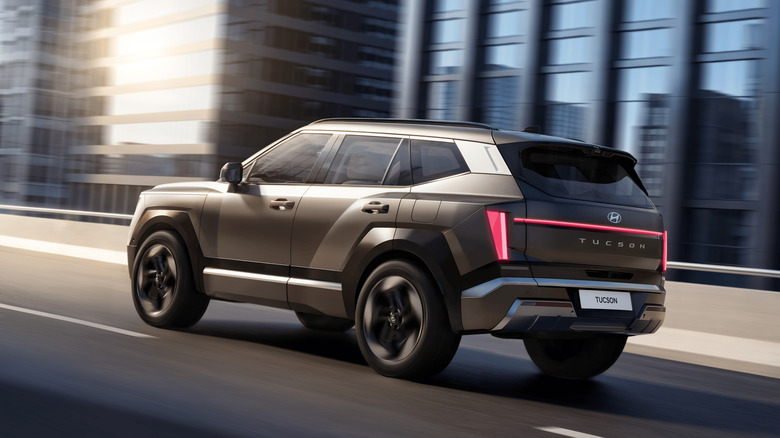 Hyundai Tuscon 2027 года движется по городскому шоссе, вид сзади слева в 3/4