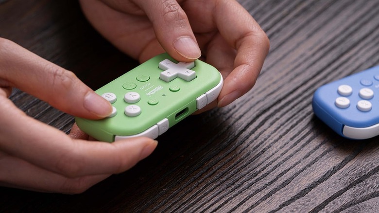 Человек, держащий контроллер 8BitDo Micro, рядом находится еще один человек.