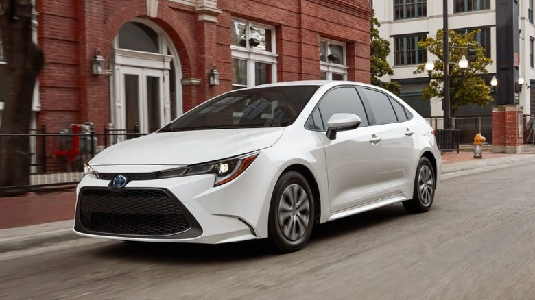 Белый Toyota Corolla Hybrid 2022 года едет по городской улице